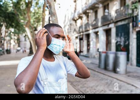 uomo afroamericano che rimuove una maschera chirurgica blu dal viso Foto Stock