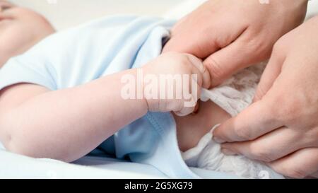 Closeup di madre che tinge fuori e cambia i pannolini disordinati del suo bambino che si trova nella culla. Concetto di igiene del genitore, del bambino e sviluppo del bambino. Foto Stock