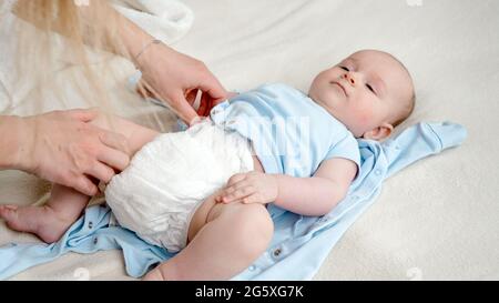 Closeup di madre che cambia pannolini sudicio a bambino figlio piccolo che si trova nel letto Foto Stock