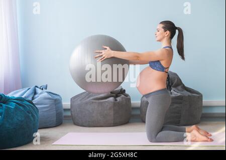 Donna europea incinta esegue esercizi con palla fitness. La madre in attesa sta facendo yoga nel 3° trimestre. Ragazza in classe in Foto Stock