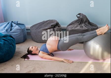 Donna europea incinta esegue esercizi con palla fitness. La madre in attesa sta facendo yoga nel 3° trimestre. Ragazza in classe in Foto Stock