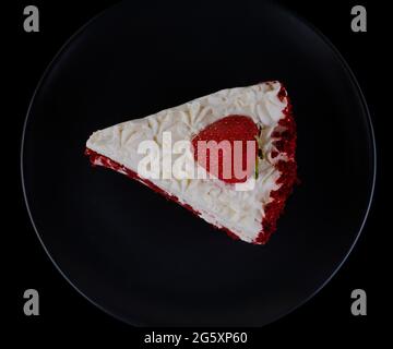 Pezzo di torta coperto di crema proteica e fragole su una piastra nera e fondo nero isolato Foto Stock