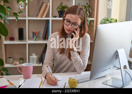 Donna impegnata che lavora a casa e utilizza il telefono cellulare Foto Stock