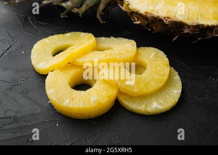 Set di tagli freschi di ananas a fette, su sfondo nero scuro del tavolo in pietra Foto Stock