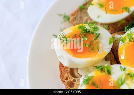 Metà uova sode con aneto su pane tostato a grani interi su un piatto bianco. Primo piano, vista dall'alto. Concetto di colazione sano, sano e sano Foto Stock