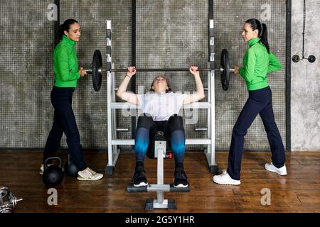 Pressa da panca su donne di addestramento in palestra, giovane donna che fa l'esercitazione del barbell con l'aiuto degli assistenti. Foto Stock