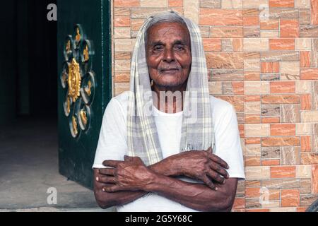 Anziano indiano maschio con i capelli grigi che portano sciarpa grigia sopra la testa e le braccia ripiegate pose fuori della sua casa, Trichy, Tamil Nadu, India Foto Stock