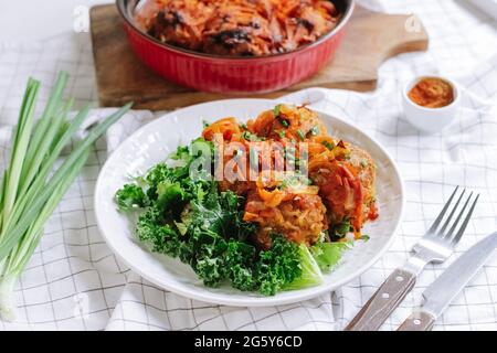 porzione di polpette cotte al forno con verdure e foglie di insalata su un piatto bianco. pasto cotto in casa. cosparso di scalione. interno tavolo da cucina. Foto Stock