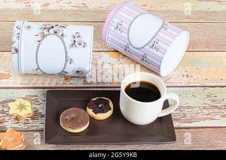 Biscotto alla burreria con un fiore secco sopra, accanto ad altri biscotti, tazza di caffè e lattine sdraiati. Foto Stock