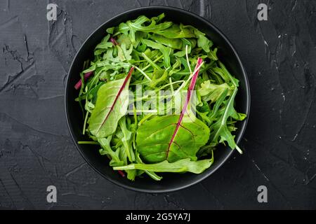 Mix di foglie di insalata, bietole svizzere e set di Arugula, su fondo di pietra nera, vista dall'alto in piano, con spazio per la copia del testo Foto Stock