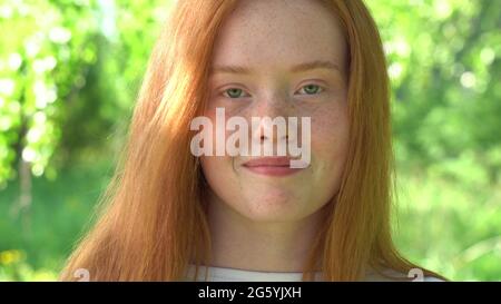 Il volto di una bella ragazza dai capelli rossi in controluce. Ritratto una giovane donna sorridente con capelli rossi e fracelle sullo sfondo di un luminoso sole Foto Stock