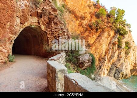 L'ingresso al tunnel Crvena Stijena si è tagliato tra le scogliere rocciose sul mare sul sentiero pedonale nella baia di Petrovac in Montenegro Foto Stock