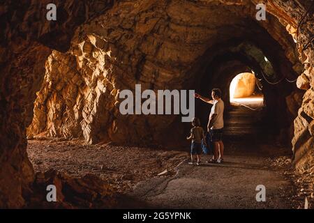 I turisti che esplorano il Tunnel si sono ritagliati nelle scogliere rocciose sul mare sul sentiero pedonale nella baia di Petrovac in Montenegro Foto Stock