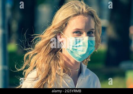 Bella bambina bionda che indossa la maschera e che cammina in città in estate durante l'emergenza Covid o Coronavirus Foto Stock