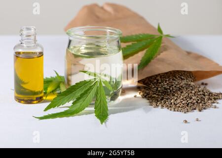 Semi di cannabis, foglie di canapa giovani e cosmetici olio CBD su sfondo bianco. Per cosmetica, trattamento, terapia. Foto Stock