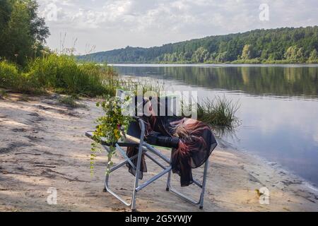 Poltrona con bouquet di fiori selvatici sulla riva del fiume Foto Stock