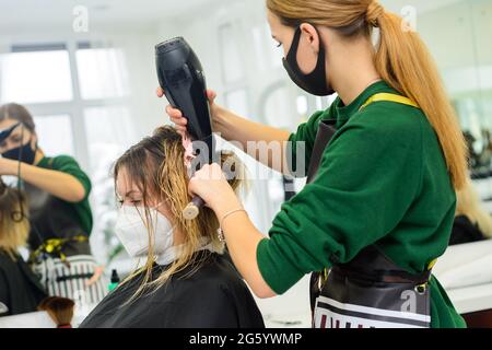 Lo stylist usa un asciugacapelli per modellare i capelli dopo la colorazione. Nuovo Foto Stock