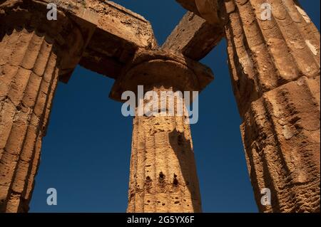 La forte luce del mattino rivela dettagli in pietra e macchie di intonaco originale su colonne doriche e capitelli scanalati in un angolo del colonnato ricostruito del Tempio e, probabilmente dedicato alla dea Hera, nell'antica città greca e porto di Selinus o Selinous a Selinunte, nella Sicilia sud-occidentale, Italia. Anche se il tempio probabilmente crollò in terremoti dopo l'abbandono di Selino, fu ricostruito nel 1958 utilizzando i materiali originali. Foto Stock