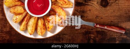 Le zeppe di patate al forno e il ketchup panorama con una forchetta, girato dall'alto su uno sfondo di legno rustico scuro Foto Stock