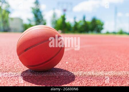 Arancione vecchio pallone da basket su un campo di gomma rossa.Sunny estate caldo giorno.blurred background.Orange palla è in attesa per lo spazio player.Copy. Foto Stock