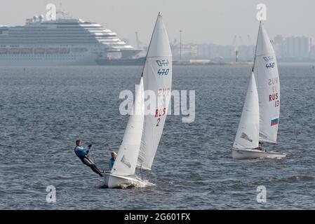 San Pietroburgo, Russia, 27 luglio 2018: Yacht di classe 470 nel Golfo di Finlandia contro grandi navi da crociera ormeggiate nella facciata del mare del porto Foto Stock