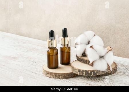 Due flaconi contagocce in vetro per uso medico e cosmetico e fiori di cotone bianco su tagli di legno. Concetto DI SPA. Foto Stock