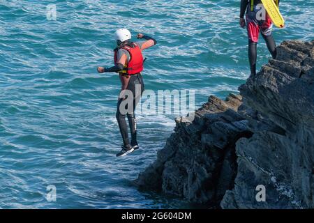 I vacanzieri saltano dalle rocce costellando con una guida su Towan Head a Newquay in Cornovaglia. Foto Stock