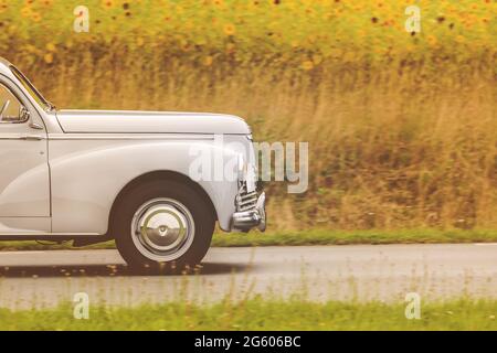 Immagine in stile retrò di un'auto degli anni '50 che guida da un campo con girasoli fioriti Foto Stock