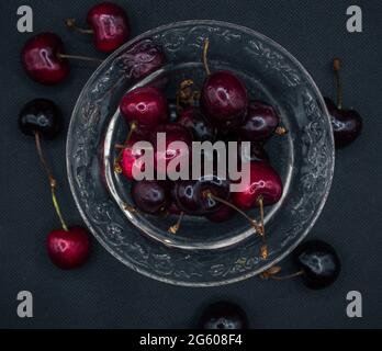 Ciliegie con gocce d'acqua in un vaso di vetro trasparente su un tavolo nero. Ciliegie mature. Dolce ciliegia rossa. Vista dall'alto. Stile rustico. Carta da parati di frutta Foto Stock