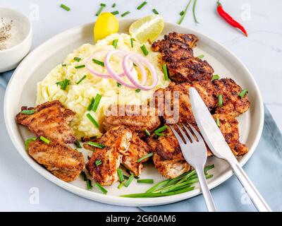 Cosce di pollo grigliate con purè di patate guarnite con erba cipollina e limone Foto Stock