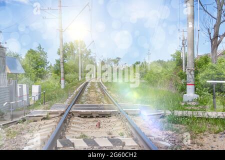 La ferrovia che va in lontananza. Attraversamento ferroviario con alberi verdi e cielo blu in estate. Foto Stock