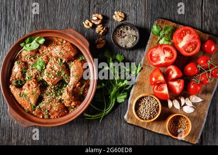 Chakhokhbili, pollo stufato, pomodoro con erbe fresche, noci e spezie in una pentola di argilla su un tavolo di legno con ingredienti su un tagliere, georgia Foto Stock