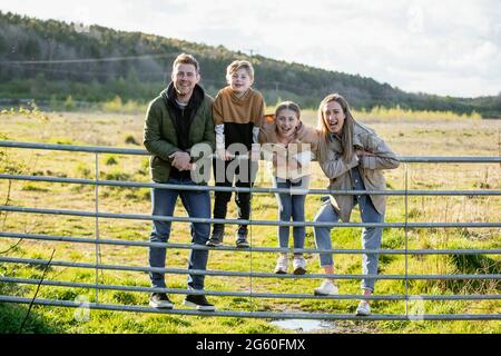 Una foto frontale di una madre e di un padre caucasici con loro figlio e figlia, tutti sorridono e guardano la macchina fotografica, mentre indossano cl casual Foto Stock