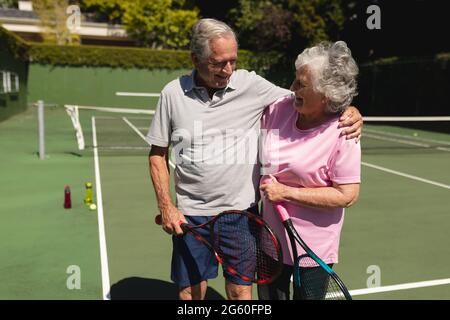 Coppia caucasica senior abbracciando e sorridendo sul campo da tennis Foto Stock