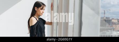 giovane donna armena che ascolta musica in cuffia guardando attraverso la finestra, banner Foto Stock