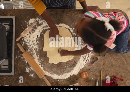 Alto angolo di madre afroamericana e figlia in cucina tagliando le forme in pasta insieme Foto Stock