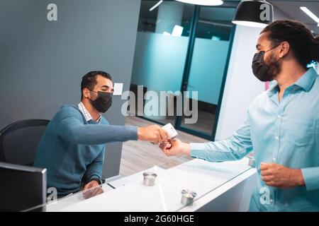 Due uomini d'affari diversi che indossano maschere al ricevimento Foto Stock