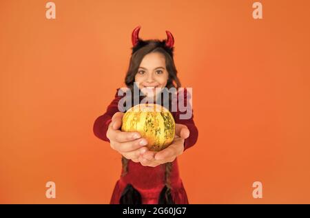 verdura di zucca nelle mani di felice diavolo capretto indossare corna costume di imp su festa di halloween, fuoco selettivo, cibo di halloween Foto Stock