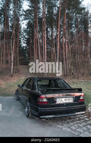 Goleniow, Polonia - 20 aprile 2021: Vecchia Mercedes Benz classe C (modello W202) sintonizzata nera vicino alla foresta. Icona berlina compatta e di lusso degli anni '90. Verticale Foto Stock