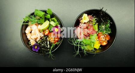 Insalate di poke con tonno e manzo in ciotole sul tavolo. Due ciotole di insalata di poke con bastoncini su sfondo grigio. Concetto asiatico di insalata di pesce Foto Stock