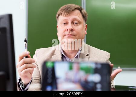 Un insegnante di chimica alla sua scrivania in classe scolastica conduce una lezione da remoto. Foto Stock