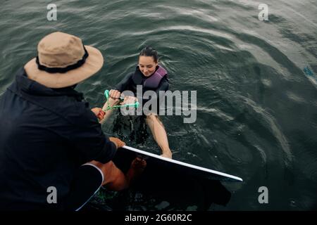 L'istruttore insegna la tecnica di wakesurf della giovane donna e impara come alzarsi in piedi sulla tavola da surf mentre tiene la corda di traino. Foto Stock