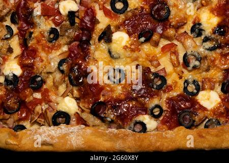 Pizza di carne con formaggio, olive e pomodori condita con salsa con il bordo dell'impasto dal fondo Foto Stock