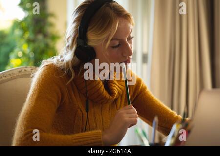 Donna caucasica che lavora in salotto a casa, indossando le cuffie e utilizzando il computer portatile, concentrandosi Foto Stock