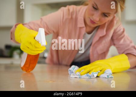 Donna caucasica che indossa guanti in gomma per pulire il piano di lavoro  della cucina con panno e spray Foto stock - Alamy