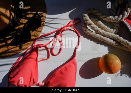 Borsa da spiaggia, occhiali da sole, bikini, cappello di paglia, orecchini, frutta arancione in foglie di palma ombra su sfondo bianco. Appartamento estivo posato. Concetto di vacanza Foto Stock