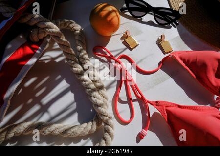 Borsa da spiaggia, occhiali da sole, bikini, cappello di paglia, orecchini, frutta arancione in foglie di palma ombra su sfondo bianco. Appartamento estivo posato. Concetto di vacanza Foto Stock