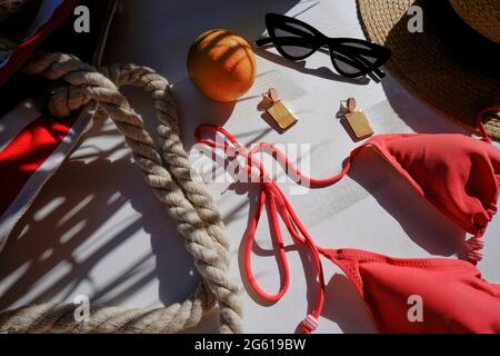 Borsa da spiaggia, occhiali da sole, bikini, cappello di paglia, orecchini, frutta arancione in foglie di palma ombra su sfondo bianco. Appartamento estivo posato. Concetto di vacanza Foto Stock