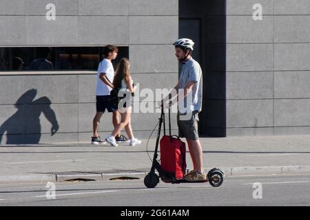 Giovane uomo con valigia gommata che guida uno scooter elettrico. Foto Stock