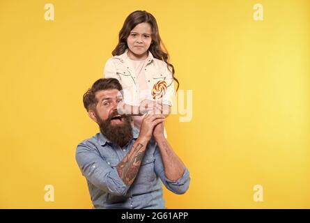 Dalo a me. Infelice bambino prendere caramella dalle mani dei padri. Negozio di caramelle. Lollipop o sucker sul bastone. Dolcetto. Fabbrica di caramelle e dolciumi Foto Stock